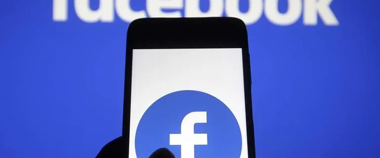 Sullo schermo di uno smartphone è raffigurato il logo di Facebook, su uno sfondo sfocato con l'iconico motivo bianco su blu, che ricorda agli utenti di impostare l'autenticazione a due fattori su Facebook per maggiore sicurezza.