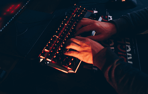 Mani che digitano su una tastiera retroilluminata con luce rossa in una stanza buia, che ricorda una configurazione Kali Linux.