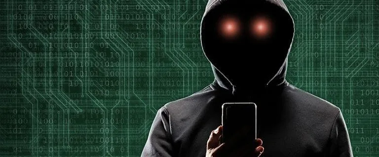Una persona che indossa una giacca con cappuccio usa uno smartphone, probabilmente cercando di tenere in sicurezza uno smartphone Android. Il volto dell'individuo è nascosto nell'ombra, con occhi rossi luminosi visibili. Sullo sfondo, un modello di circuito digitale aggiunge un'aria di mistero.
