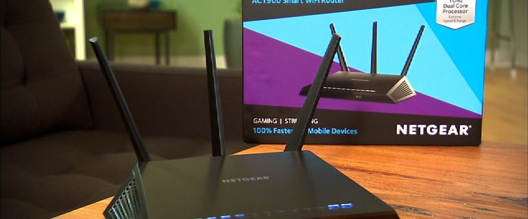 Un router WiFi intelligente Netgear Nighthawk AC1900 è appoggiato su un tavolo di legno, pronto a migliorare la tua connettività. Con tre antenne e indicatori LED blu, promette prestazioni superiori. La scatola del prodotto, che mostra l'immagine e le specifiche del router, offre spunti su come risolvere i problemi di brick del Netgear R7000.